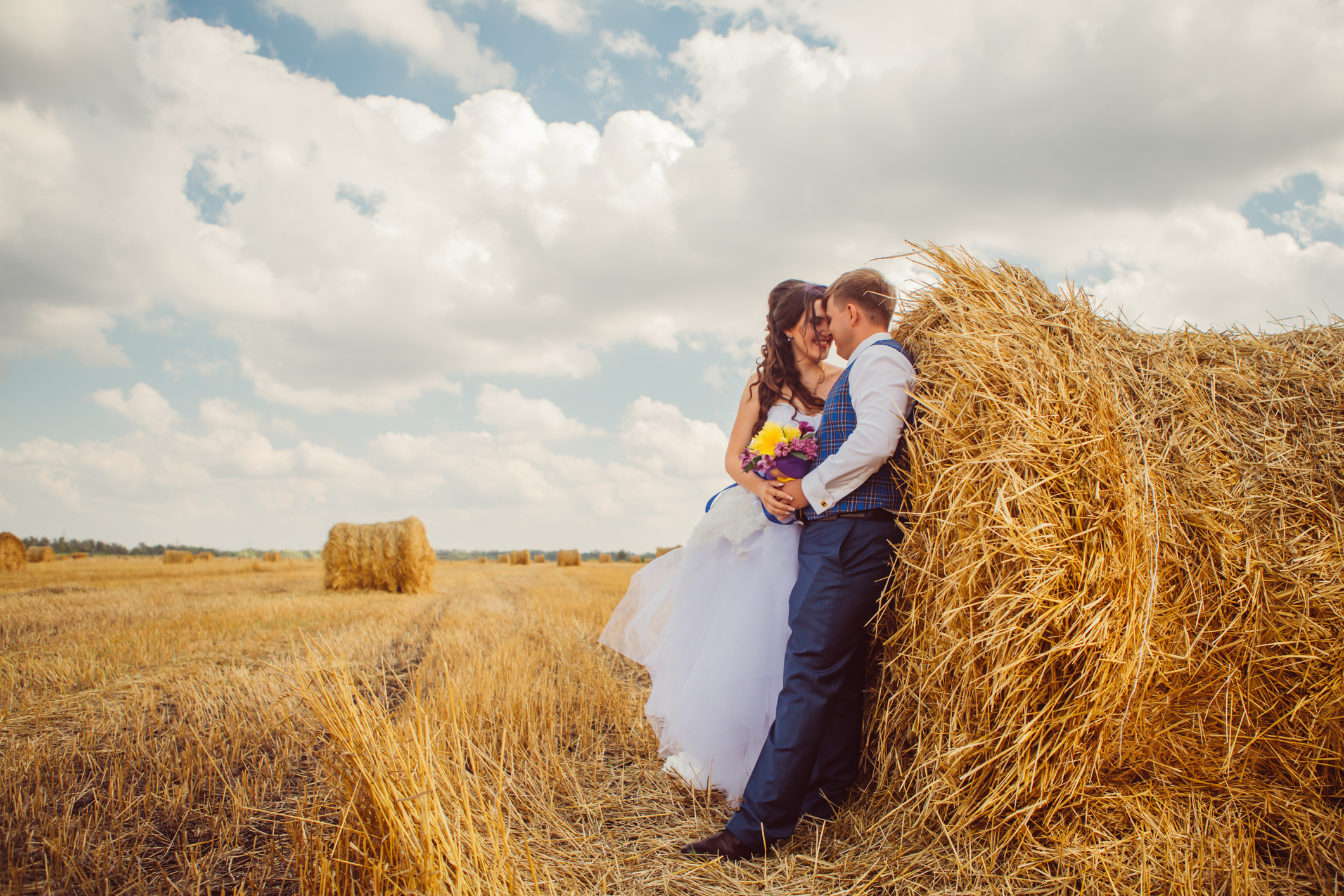 Bride and Groom leaning against round bale